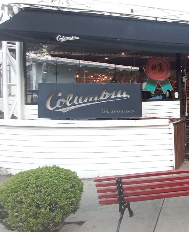 A placa Columbia Burgers na mureta branca, com a entrada do salão ao lado